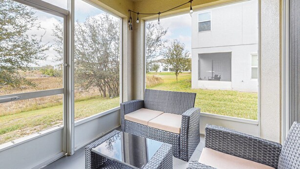 Un espace extérieur aménagé, abrité et doté de meubles en osier et d’une table en verre, offrant une vue sur une pelouse et un bâtiment.