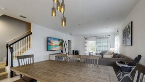 Amplia sala de estar con una mesa de comedor de madera, una escalera y un gran ventanal con cortinas.