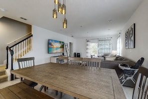 Ein geräumiges Wohnzimmer mit einem Holzesstisch, einer Treppe und einem großen Fenster mit Vorhängen.