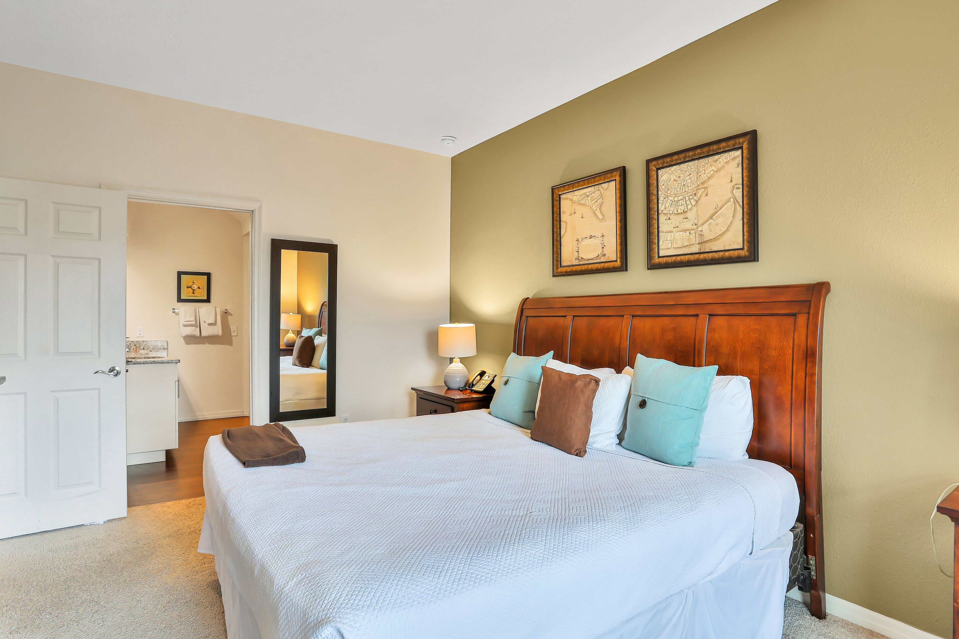 A neatly made bed with a wooden headboard, a bedside table with a lamp, and a framed map on the wall.