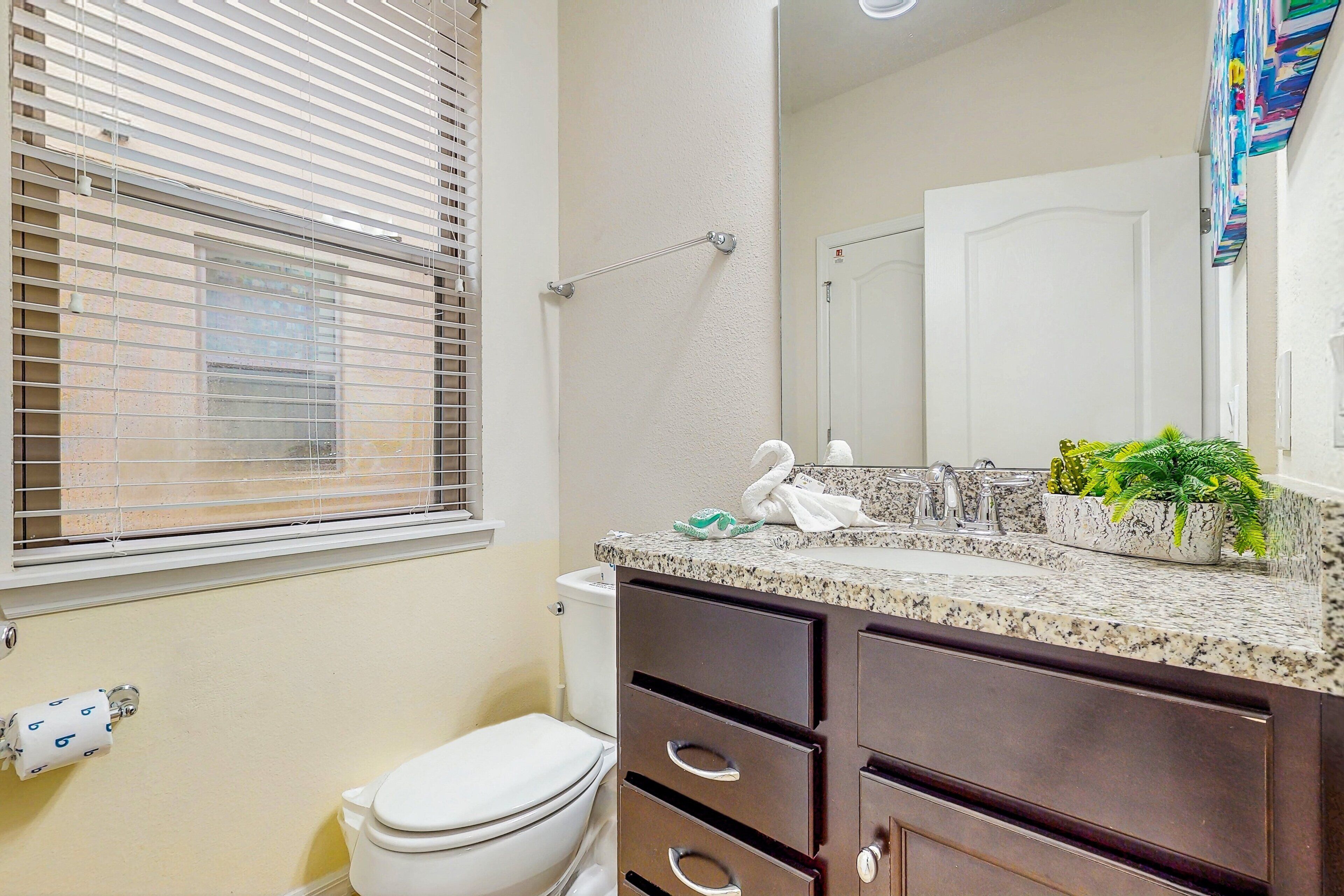 A bathroom with a toilet, a towel rack, a mirror, and a countertop with a plant.