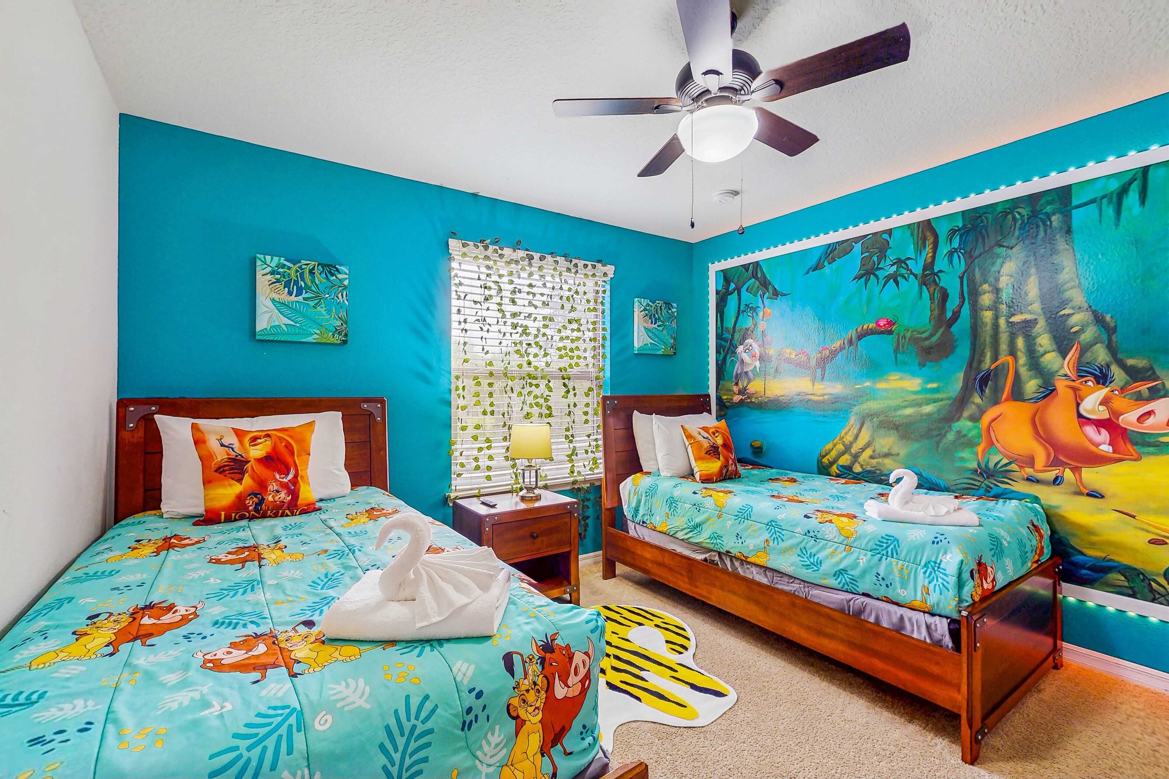 A bedroom with two beds, a ceiling fan, a window with blinds, and a mural on the wall.