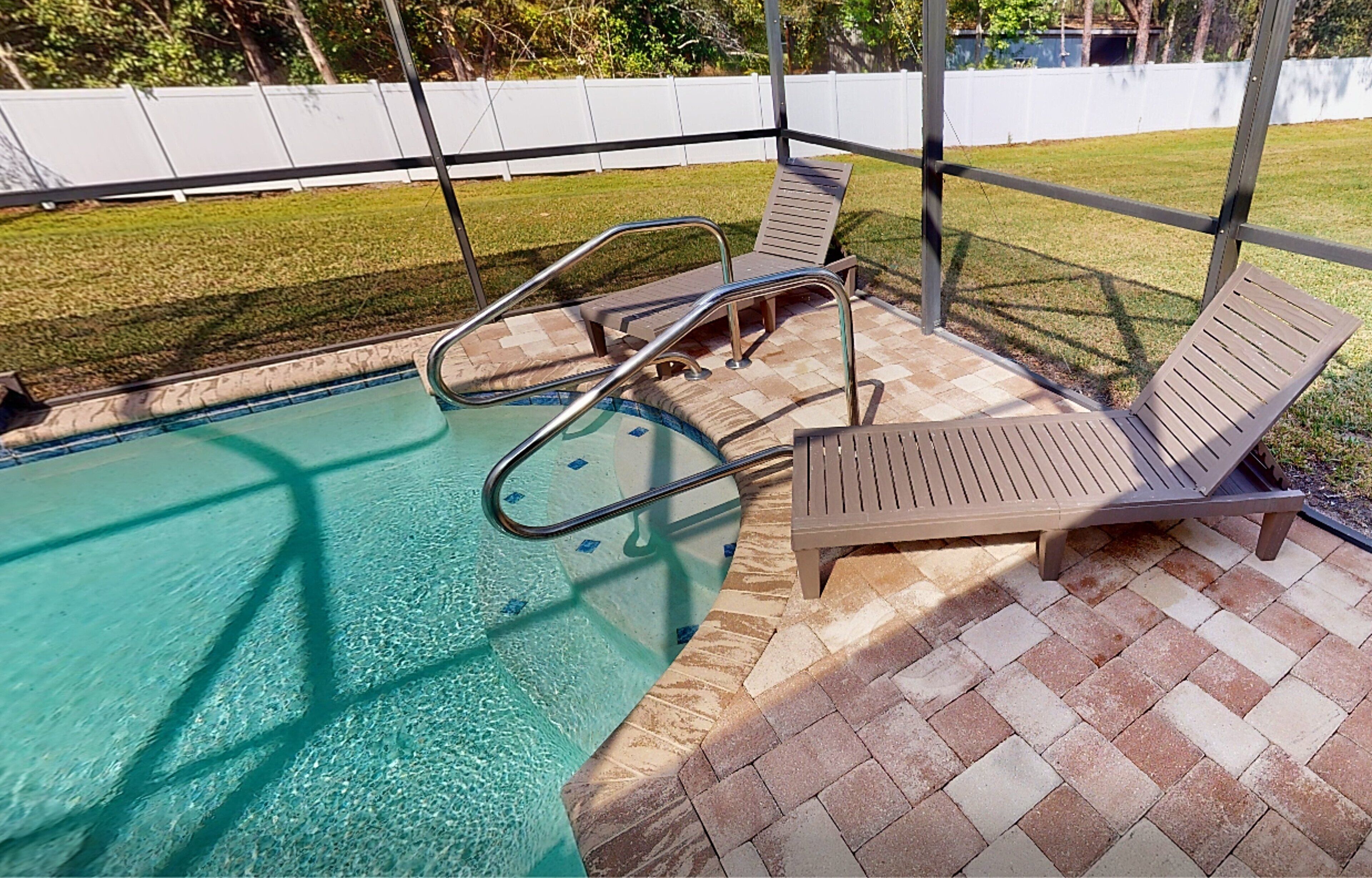 Una piscina con plataforma de baldosas, barandillas de metal y dos sillas reclinables.