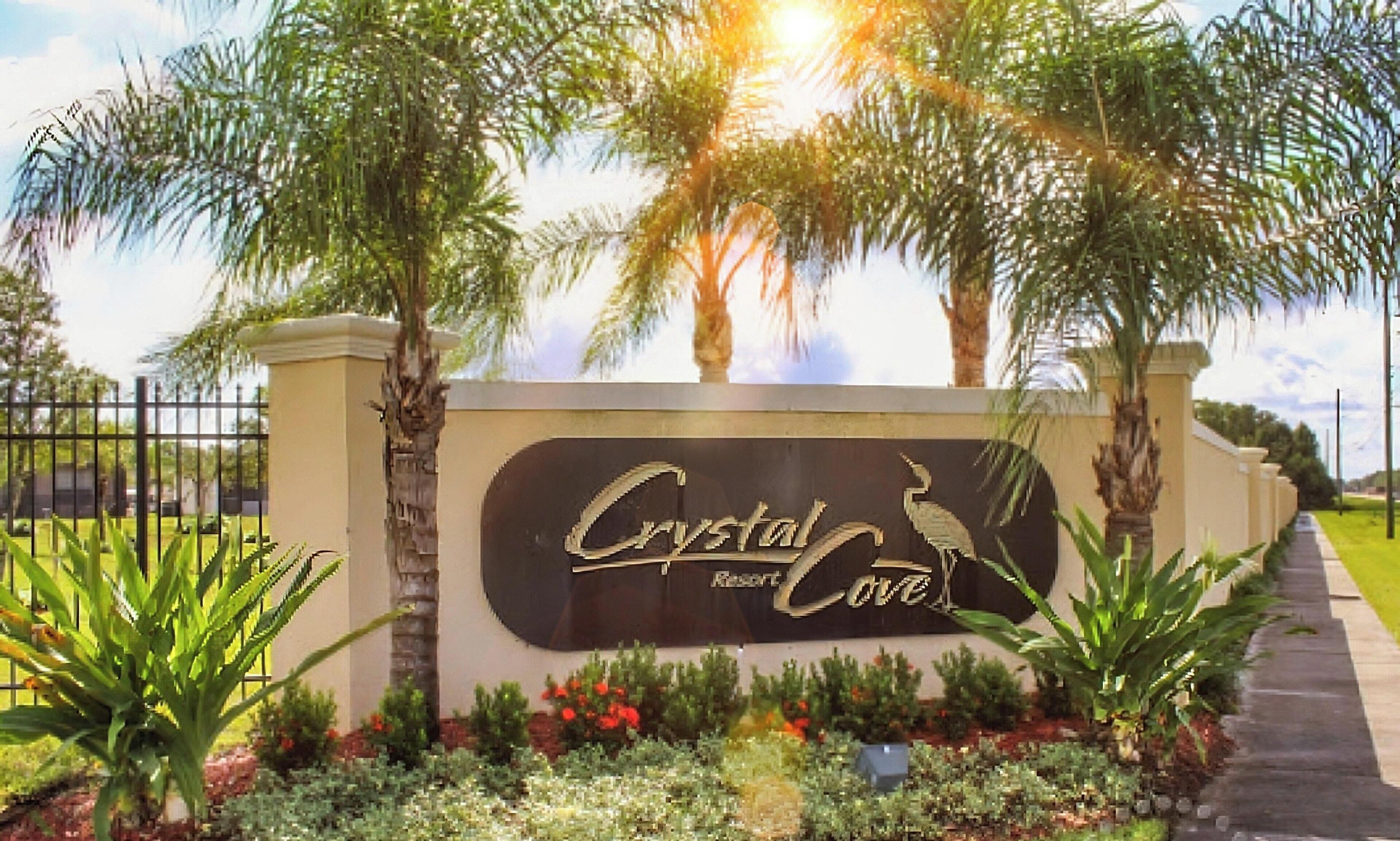 A sign for Crystal Resort & Cove with a bird logo, surrounded by palm trees and a landscaped garden.