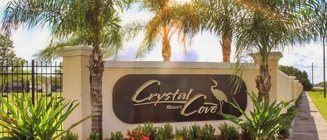 A sign for Crystal Resort & Cove with a bird logo, surrounded by palm trees and a landscaped garden.