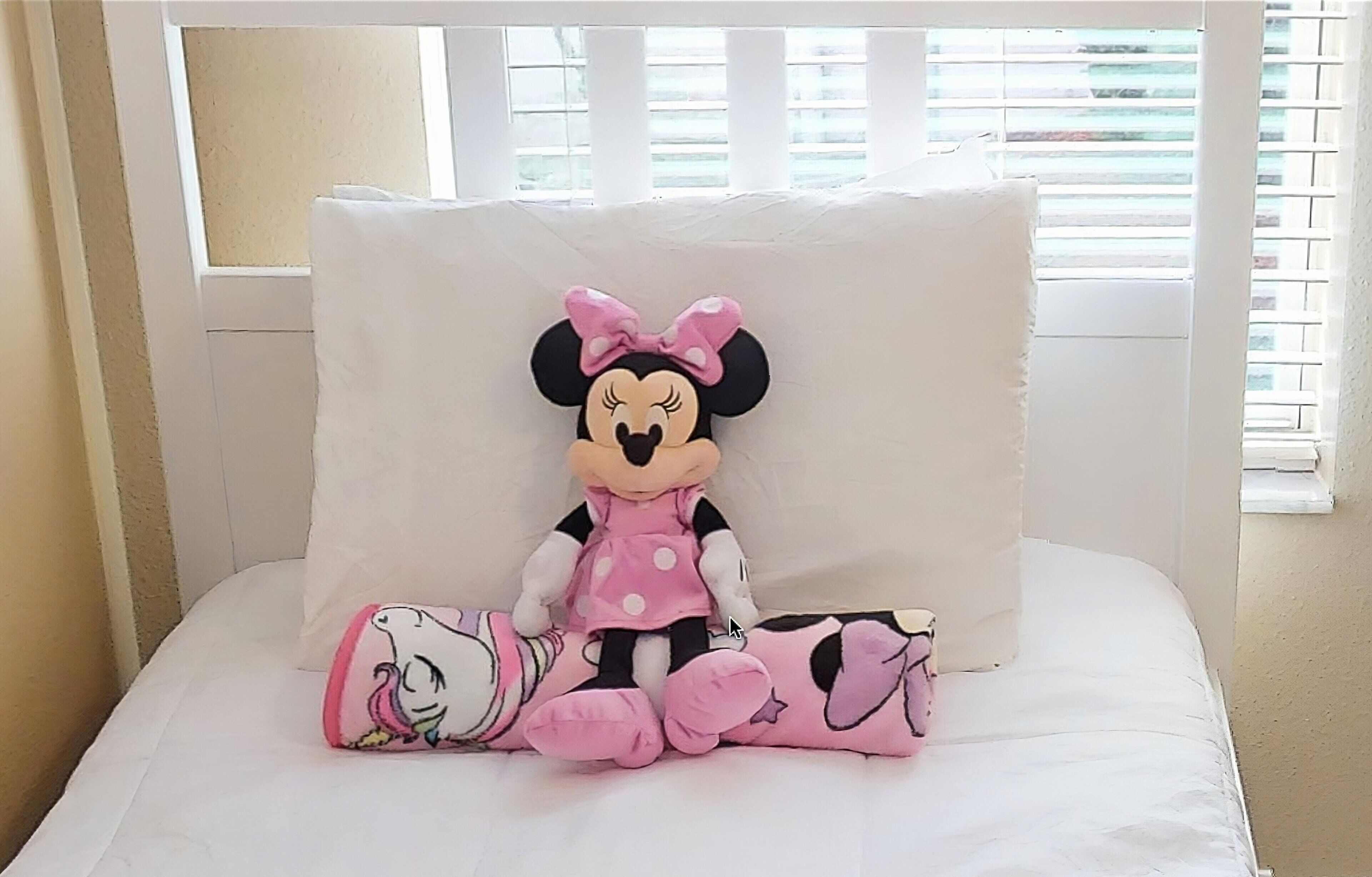Ein Bett mit einem kuscheligen Minnie Maus Spielzeug und passendem Kopfkissen.