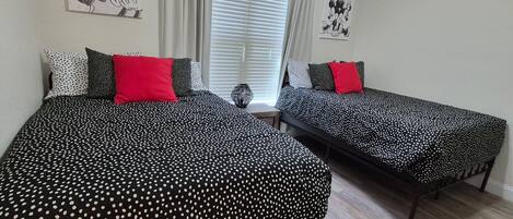 Une chambre avec deux lits, chacun agrémenté de draps à pois noirs et blancs et d’oreillers rouges. Au-dessus des lits, on trouve des décorations murales représentant Mickey Mouse.