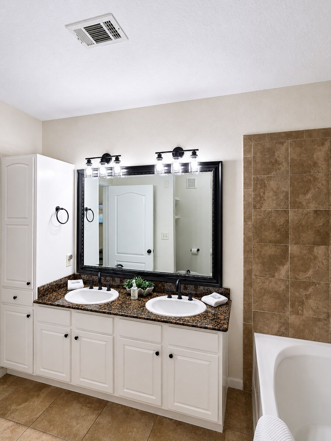 Une salle de bain avec deux lavabos, un grand miroir, un meuble-lavabo, une baignoire et un espace douche.