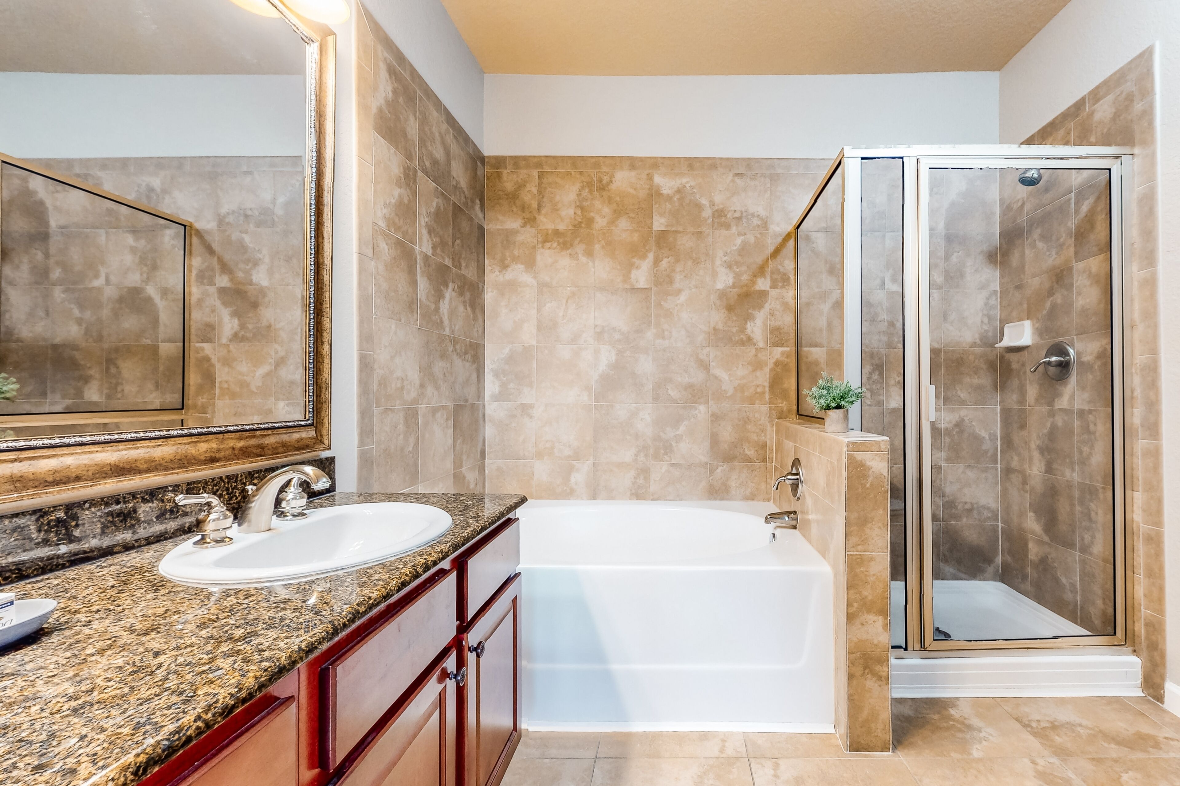 A bathroom with a granite countertop, a white sink, a bathtub, and a glass-enclosed shower.