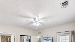 Une chambre à coucher comprenant un lit, un ventilateur de plafond, une télévision et une porte donnant sur une salle de bain.