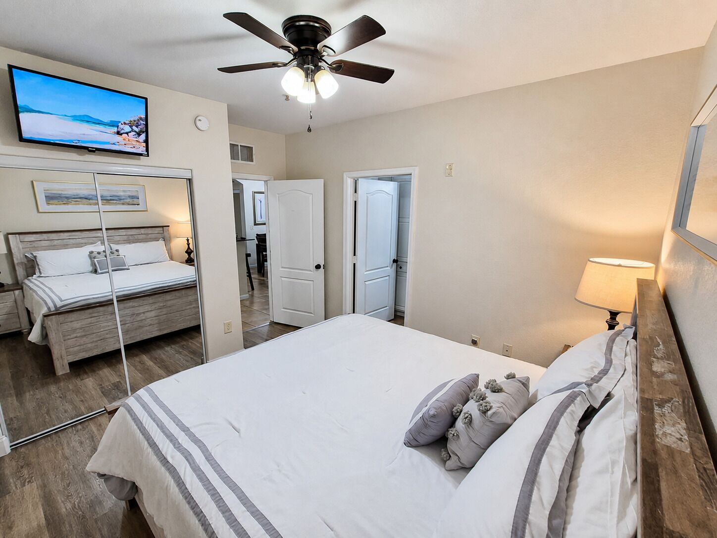 Une chambre à coucher comprenant un lit, un ventilateur de plafond, un téléviseur et une porte donnant sur une autre pièce.