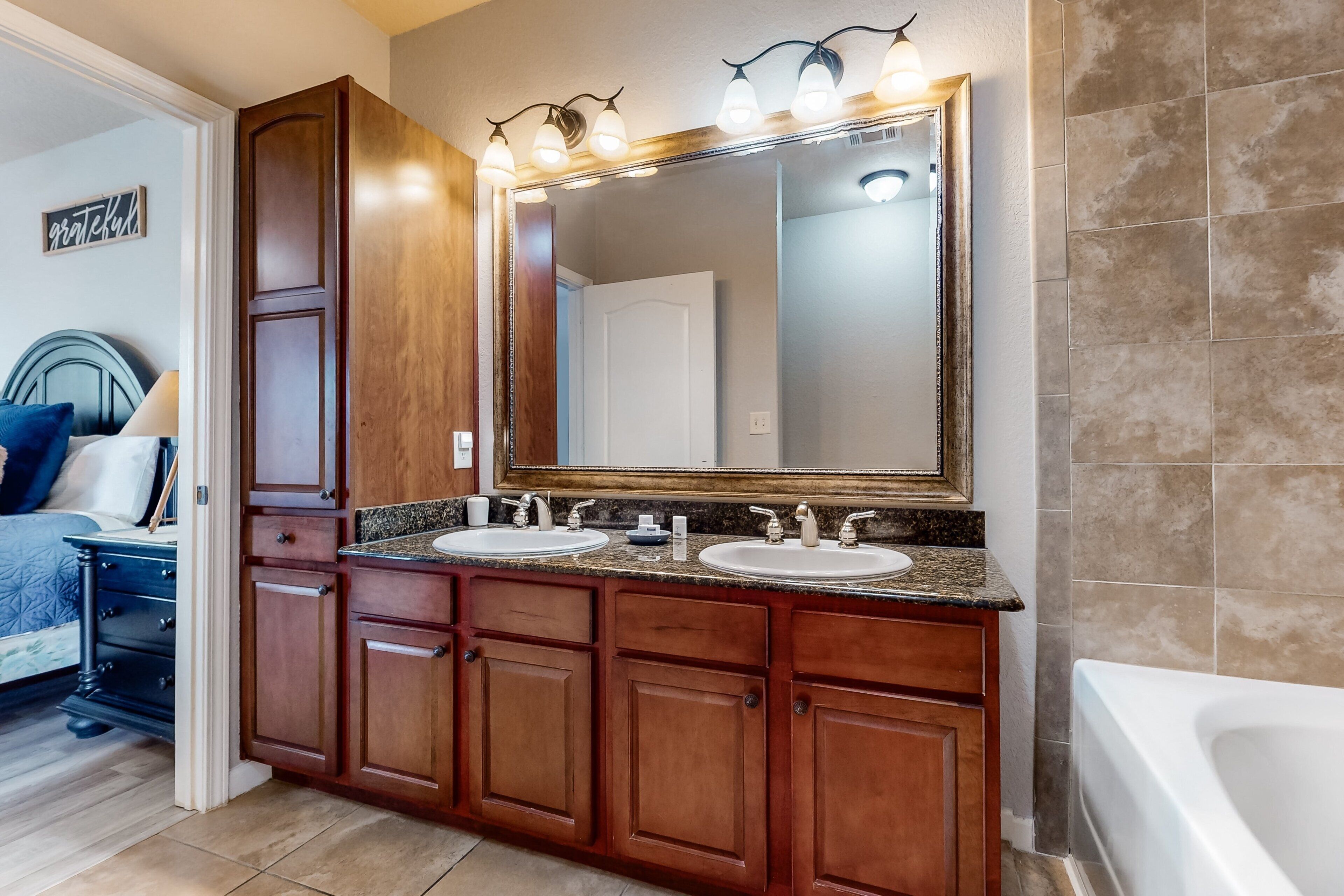 A bathroom with a large mirror, two sinks, wooden cabinets, and a bathtub.