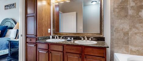 A bathroom with a large mirror, two sinks, wooden cabinets, and a bathtub.