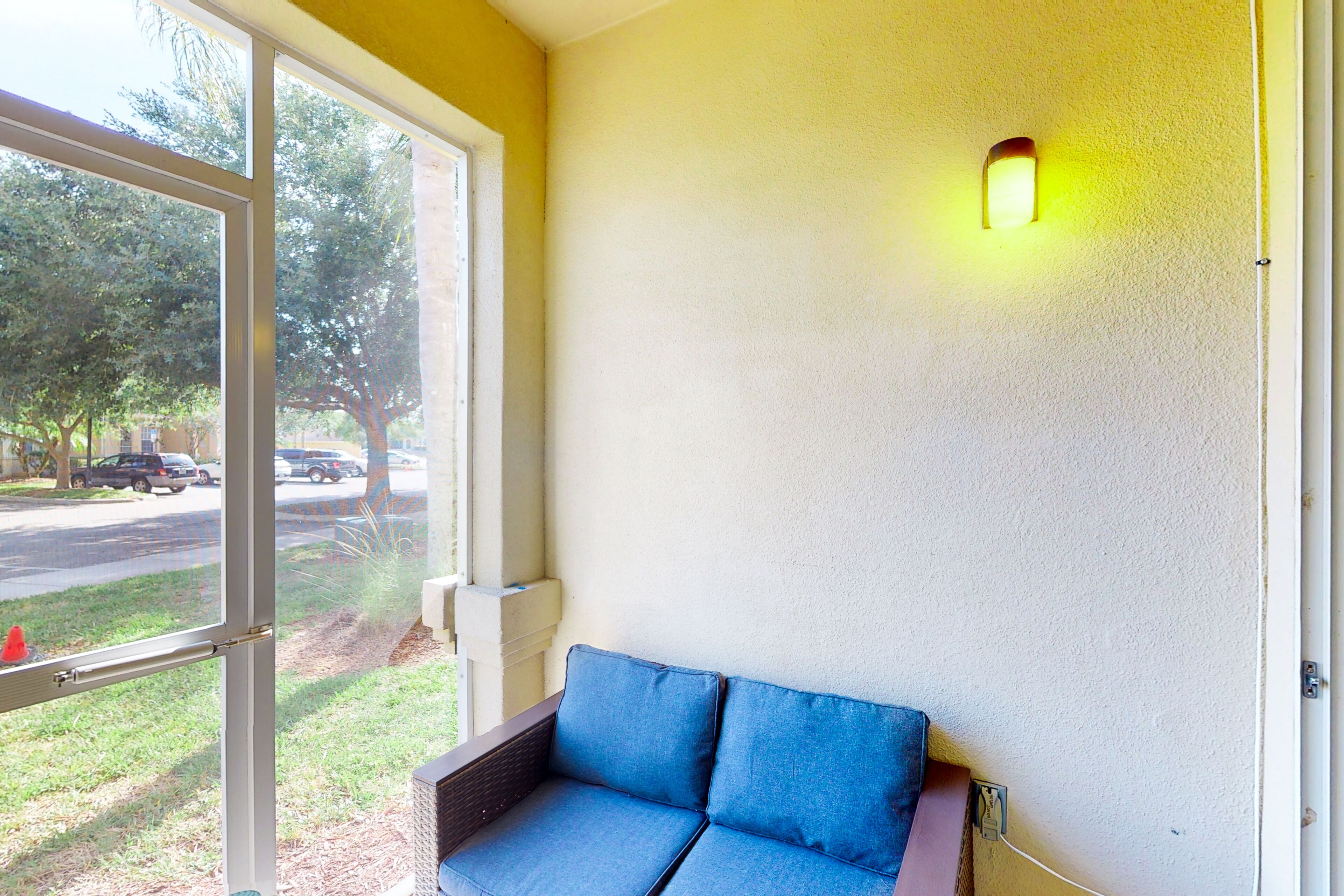 Une pièce avec un canapé bleu, une grande fenêtre et un luminaire fixé au mur.