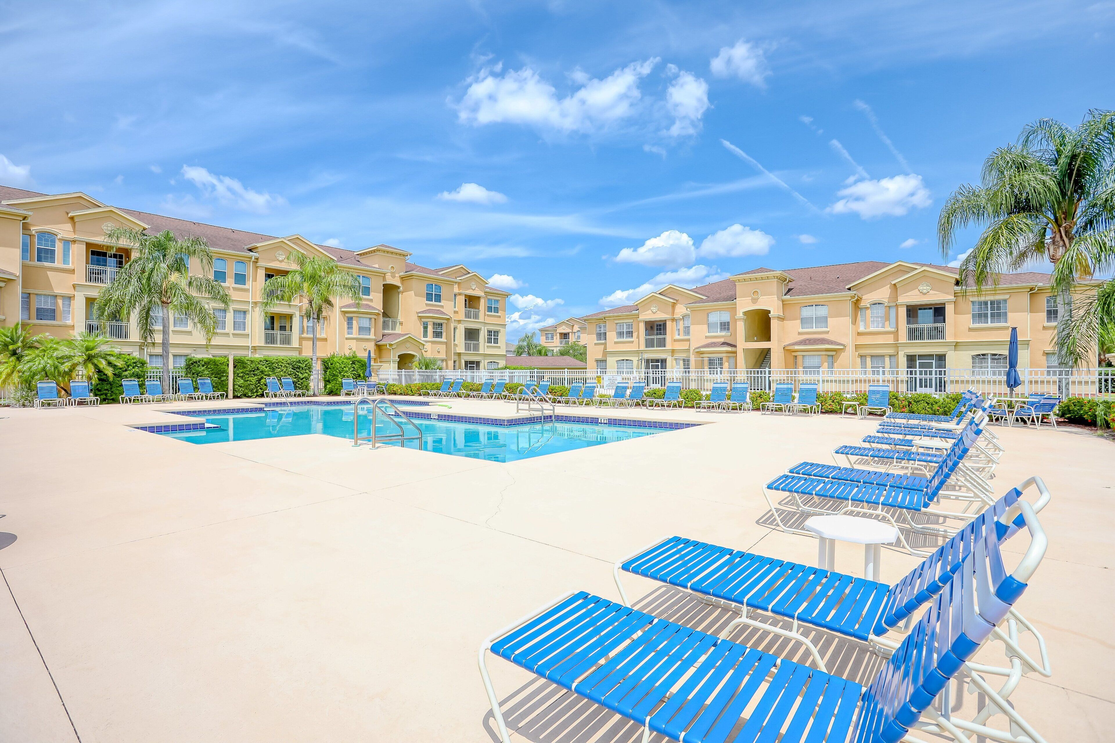 A hotel with a swimming pool, lounge chairs, and palm trees.