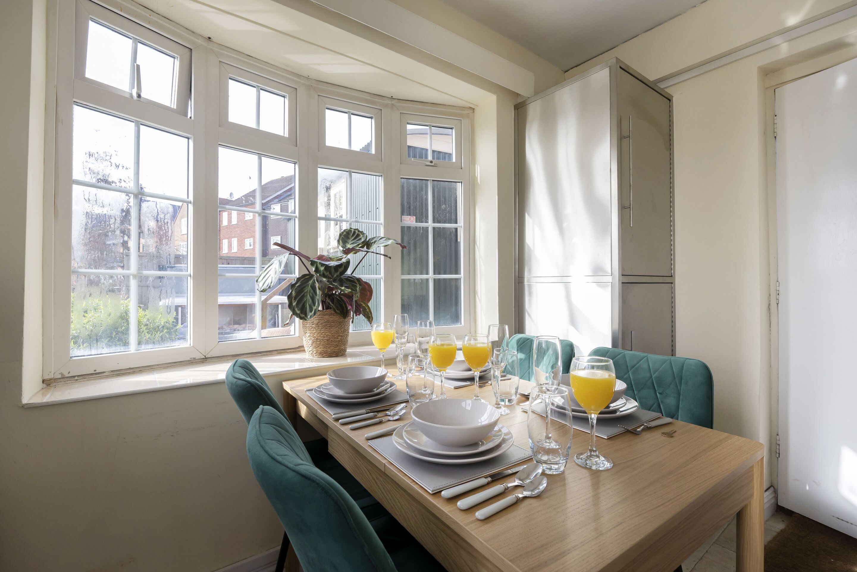 Comedor con una mesa dispuesta para cuatro, ventanas amplias y una planta en maceta.