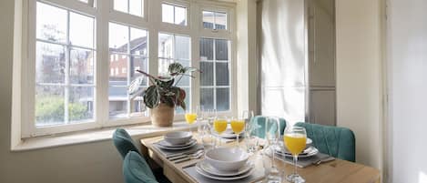 A dining area with a table set for four, large windows, and a potted plant.