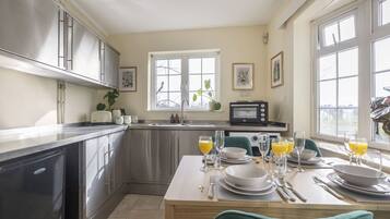 A modern kitchen with stainless steel appliances, a dining table set for four, and large windows providing natural light.