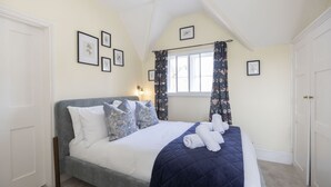 Ein ordentlich eingerichtetes Schlafzimmer mit einem Bett, einem Fenster mit Vorhängen und gerahmten Bildern an der Wand.