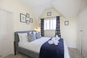 A neatly arranged bedroom with a bed, a window with curtains, and framed pictures on the wall. - Riverside Cottage and Shepherd’s Hut with Hot Tub (Tewkesbury)