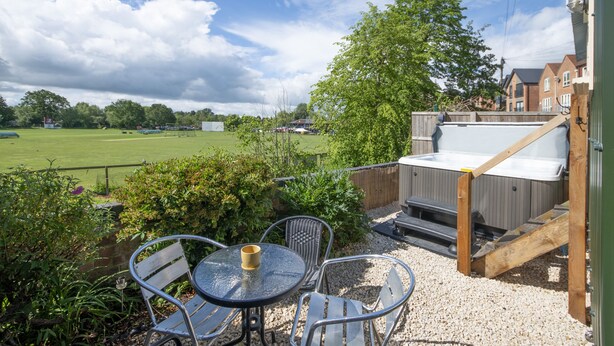 Eine Terrasse mit Whirlpool, Sitzgelegenheiten im Freien und Blick auf ein grünes Feld.
