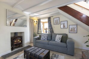 A cozy living room with a sofa, a fireplace, a mirror, and framed pictures on the wall. - Riverside Cottage and Shepherd’s Hut with Hot Tub (Tewkesbury)
