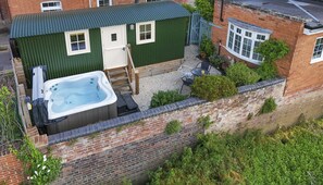 A hot tub, a small shed, and a brick wall with vegetation. - Riverside Cottage and Shepherd’s Hut with Hot Tub (Tewkesbury)