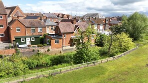 A residential area with brick houses, a green-roofed structure, and a grassy area with a fence. - Riverside Cottage and Shepherd’s Hut with Hot Tub (Tewkesbury)