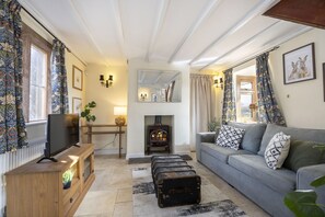 A cozy living room with a fireplace, a sofa, a television, and a wooden cabinet. - Riverside Cottage and Shepherd’s Hut with Hot Tub (Tewkesbury)