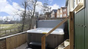 A hot tub in a backyard with a wooden deck, a wooden staircase, and a green metal door.