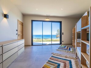 A spacious hallway with a view of the ocean, a sliding glass door, and a wooden bookshelf. - Villa Sari Di Solenzara (Sari-Solenzara)