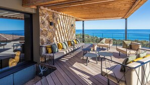Eine Holzterrasse mit Sitzgelegenheiten im Freien, eine Steinmauer und Blick aufs Meer.