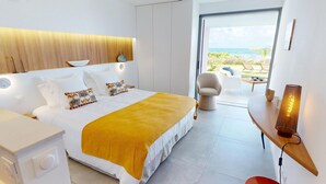 Ein modernes Schlafzimmer mit einem Bett, Nachttischen, einem Sessel und Meerblick.