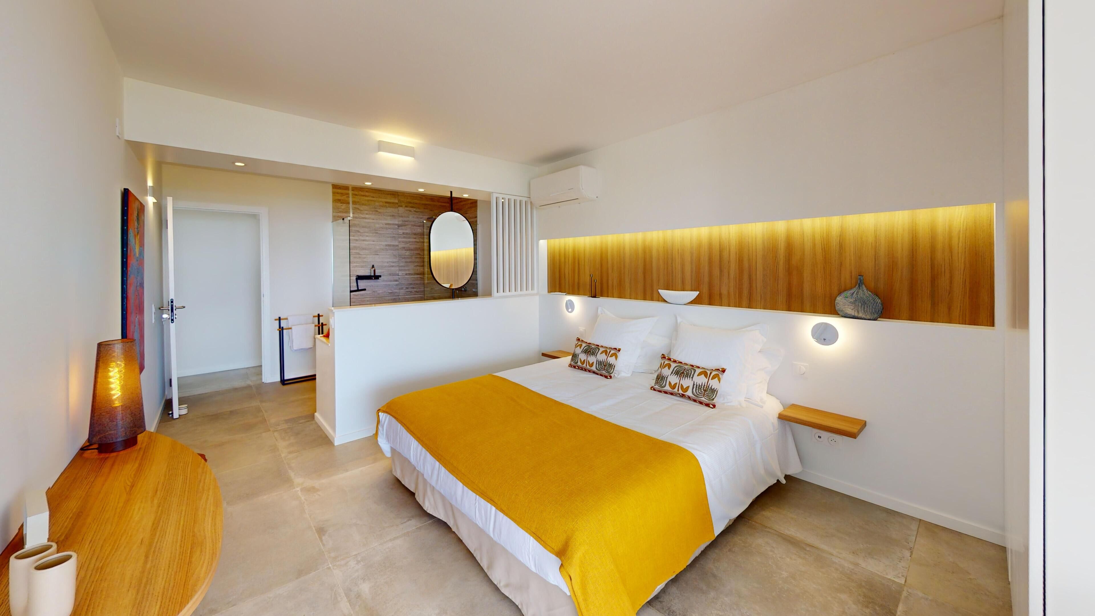 A modern bedroom with a large bed, bedside tables, a mirror, and a wooden headboard.
