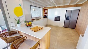 A modern kitchen with white cabinetry, a central island, and a stainless steel refrigerator. - Aqualis - Beachfront Villa in Le Moule (Aquawaves) (Le Moule)
