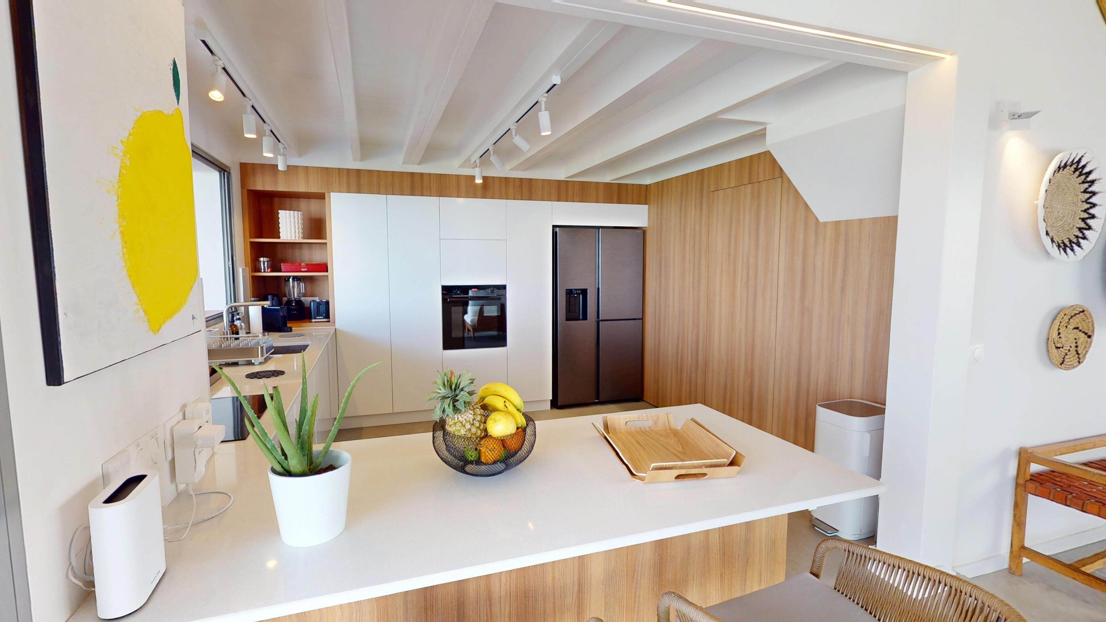 A modern kitchen with a white countertop, a built-in oven, a stainless steel refrigerator, and a potted plant.
