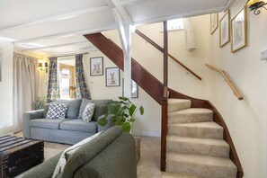 Un salon avec un canapé gris, un escalier en bois et une grande fenêtre avec des rideaux.