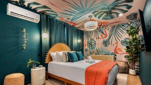 A bedroom with a bed, a bedside table, a lamp, a wall-mounted air conditioner, and a ceiling with a tropical mural. - Htd Pool, TikiHut, Pickleball, Golf, 7 mi to AMI (Bradenton)