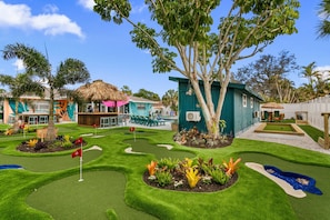 A golf course with a thatched-roof pavilion, a pool area, and a small building with a blue exterior.