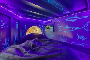 A room with a bed, a TV, and walls decorated with marine life projections.