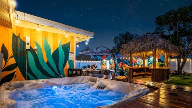 A hot tub on a wooden deck with a tropical-themed mural and a thatched-roof bar area. - Htd Pool, TikiHut, Pickleball, Golf, 7 mi to AMI (Bradenton)