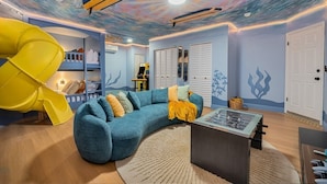 A room with a curved blue sofa, a yellow slide, and a ceiling with a starry design. - Htd Pool, TikiHut, Pickleball, Golf, 7 mi to AMI (Bradenton)