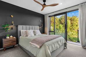 Une chambre à coucher comprenant un lit, une table de chevet, un ventilateur de plafond et une grande fenêtre donnant sur un paysage verdoyant.