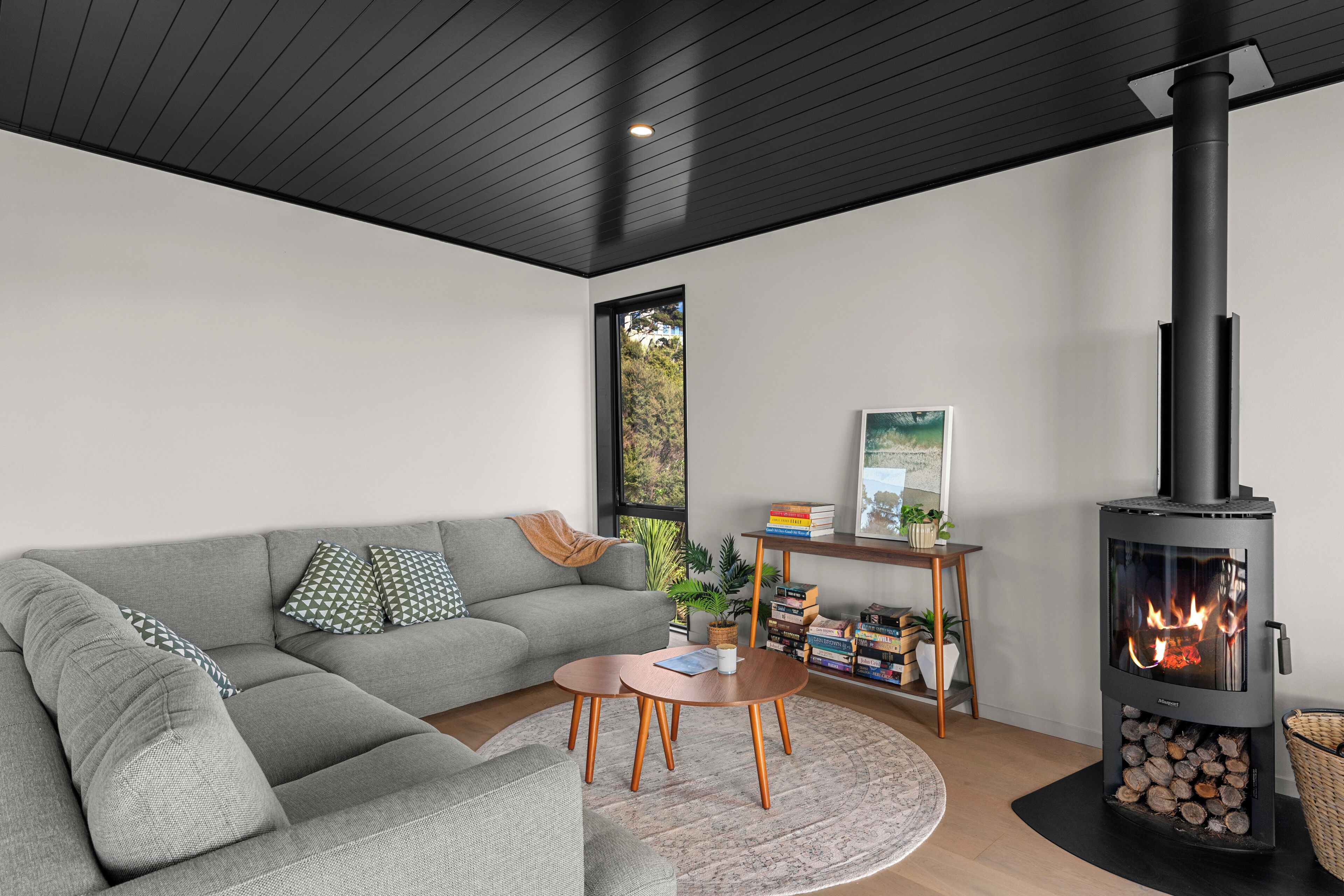 A modern living room with a grey sofa, round coffee table, and a wood-burning stove.