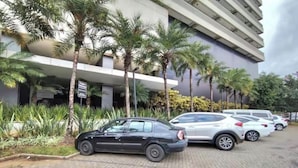 Een parkeerplaats met meerdere auto's, palmbomen en een modern gebouw met een plat dak en balkons.