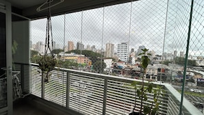 Een balkon met uitzicht op een stadsgezicht, een hangplant en een krant op de vloer.