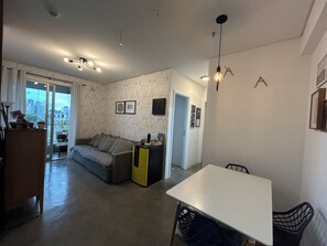 A modern living room with a sofa, a dining table with chairs, and a kitchen area with a yellow cabinet. - Confortável e estiloso apartamento completo com 2 quartos, sendo uma suíte. (Osasco)