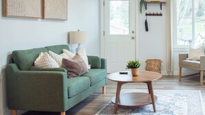 Een woonkamer met een groene bank, een ronde salontafel, een lamp en een kamerbreed tapijt met dessin.