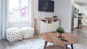 Een moderne woonkamer met een televisie, poefs, een salontafel en een keuken op de achtergrond.