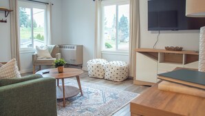 Een woonkamer met een bank, een voetenbankje, een salontafel, een televisie en uitzicht op de omgeving.